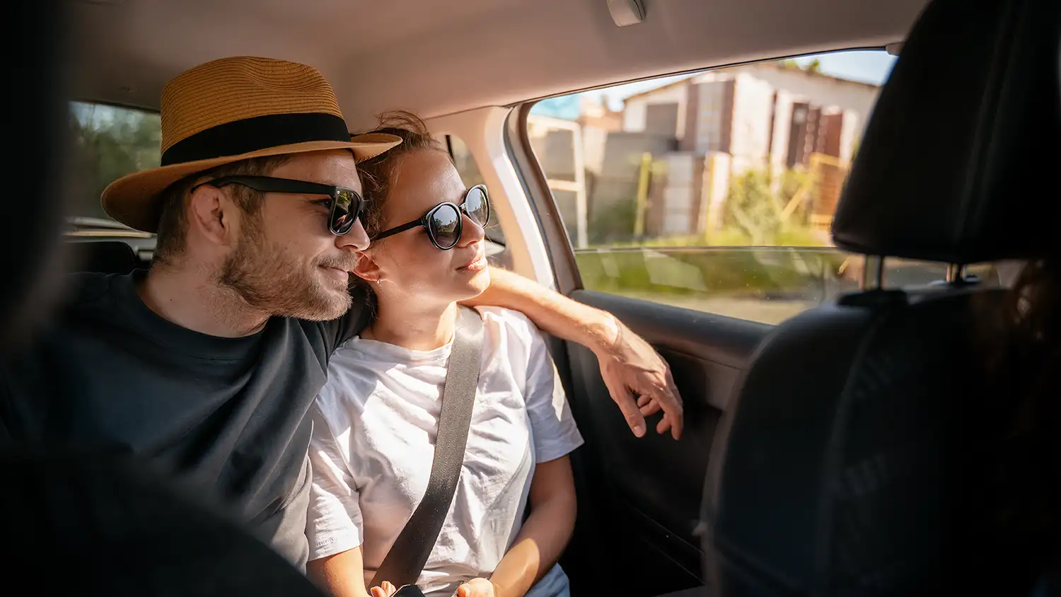 Junges, fröhliches, glückliches Paar von Reisenden, die im Auto auf dem Rücksitz sitzen und aus dem Fenster schauen